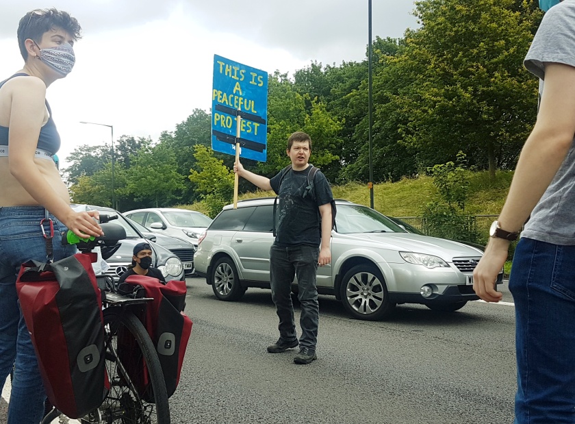 Kill The Bill on the M32 motorway. A protester stands in front of traffic with a placard reading "This is a Peaceful Protest".