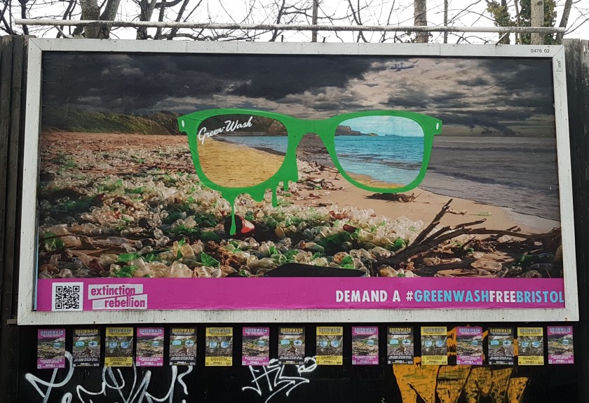 Billboard shows a pair of glasses superimposed on an image of a beach. Around the glasses the beach is covered in plastic waste; through the lenses of the glasses the beach is pristine.